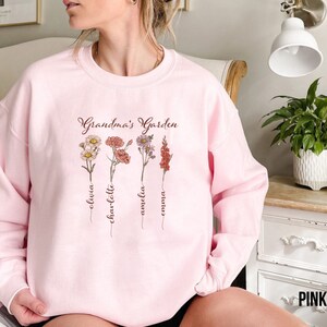 May include: Pink sweatshirt with the text "Grandma's Garden" and four floral designs with names Olivia, Charlotte, Amelia, and Emma written underneath each flower.