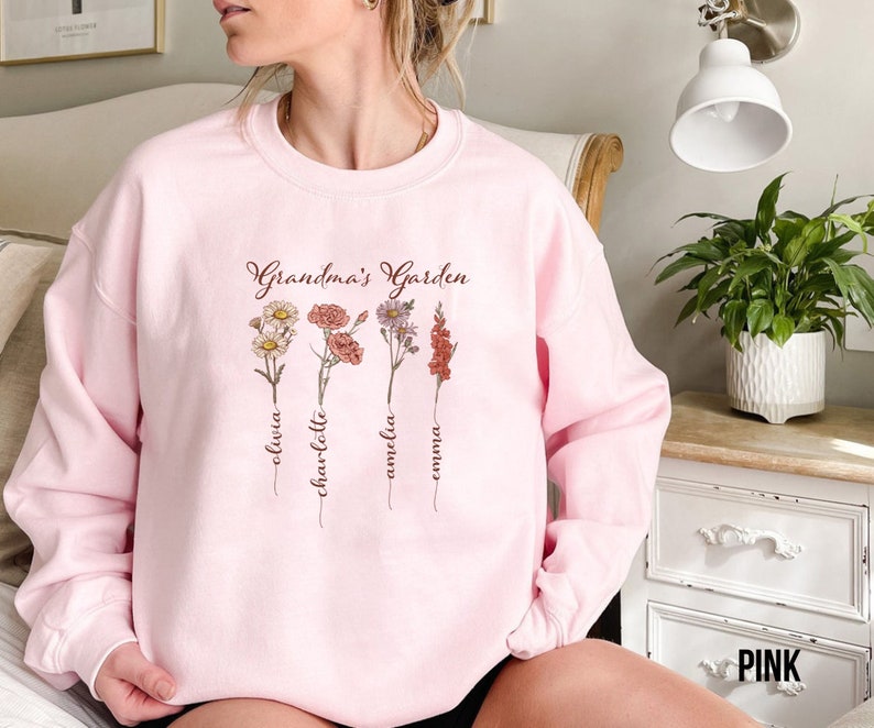 May include: Pink sweatshirt with the text "Grandma's Garden" and four floral designs with names Olivia, Charlotte, Amelia, and Emma written underneath each flower.