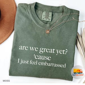 Op de afbeelding: Een groen T-shirt met de tekst "are we great yet? 'cause I just feel embarrassed" in wit gedrukt.