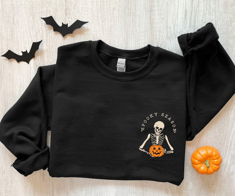 May include: Black sweatshirt with a white graphic of a skeleton holding a jack-o'-lantern. The graphic says "Spooky Season".