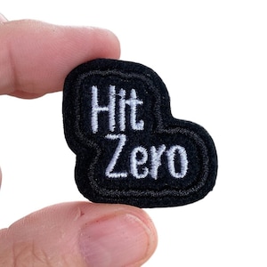 May include: Black embroidered patch with white text that reads "Hit Zero".