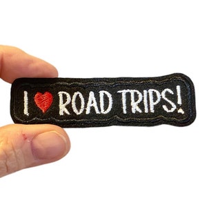 May include: Black embroidered patch with white text that reads "I love road trips!" with a red heart.