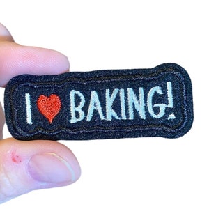 May include: A black embroidered patch with white text that says "I love baking!" and a red heart.