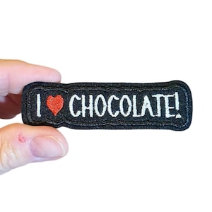 May include: Black embroidered patch with white text that reads "I love chocolate!" and a red heart.