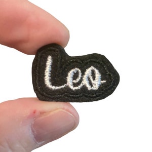 May include: A black felt patch with white embroidered lettering that reads "Leo".