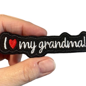Könnte beinhalten: Schwarzer Bügel-Patch mit weißer Stickerei, auf dem "Ich liebe meine Oma!" mit einem roten Herzen steht.