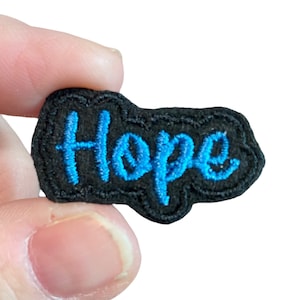 May include: A black fabric patch with a blue embroidered word "Hope" in a cursive font.