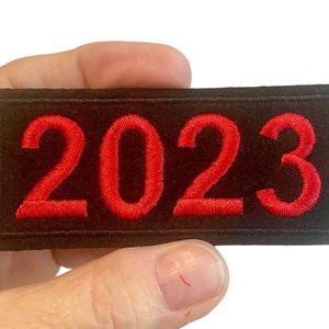 May include: Red embroidered patch with the year 2023 on a black background.