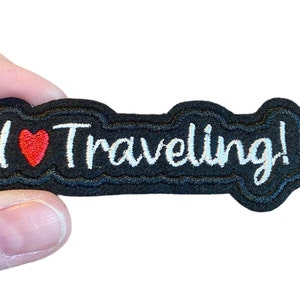 May include: Black embroidered patch with white text that says "I ♥ Traveling!" The heart is red.