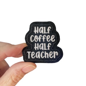 Op de afbeelding: Een zwart geborduurd embleem met de woorden "HALF COFFEE HALF TEACHER" in witte draad. Het embleem heeft een unieke, gebogen vorm en wordt tegen een witte achtergrond gehouden.