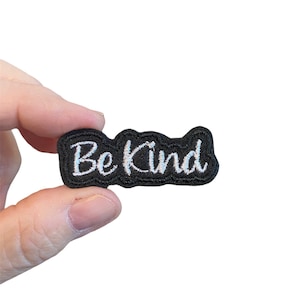 May include: Black embroidered iron-on patch with white lettering that says "Be Kind".