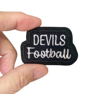 May include: Black embroidered patch with white lettering that reads "Devils Football".