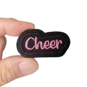 Puede incluir: Parche de fieltro negro con texto bordado en rosa que dice "Cheer".