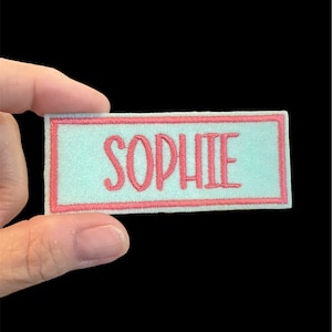May include: A light blue fabric patch with a pink border and the name "SOPHIE" embroidered in pink.