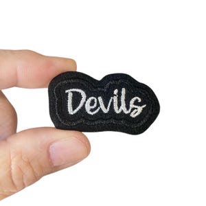May include: Black embroidered patch with white lettering that reads "Devils".