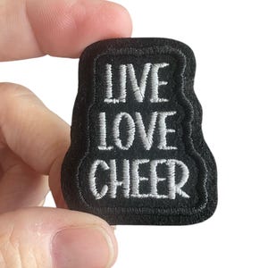 May include: Black iron-on patch with white embroidered text that reads "Live Love Cheer".