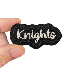 May include: A black embroidered patch with the word "Knights" in white cursive lettering.
