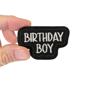 May include: Black felt patch with white embroidered text that reads "Birthday Boy".