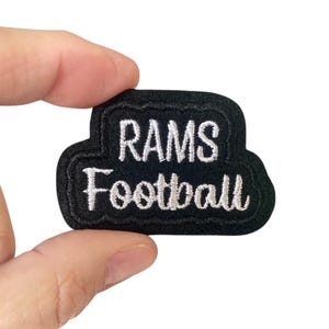 May include: Black and white embroidered patch with the text "RAMS Football" in a white cursive font.