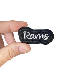 Op de afbeelding: Zwarte viltpatch met witte geborduurde tekst "Rams".