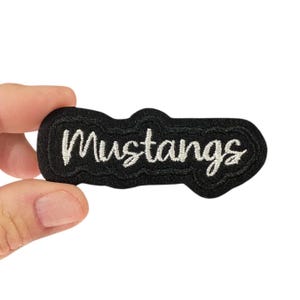 Op de afbeelding: Zwarte viltpatch met witte geborduurde tekst die "Mustangs" zegt.