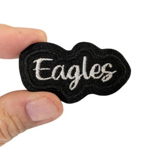 May include: Black embroidered patch with white lettering that reads "Eagles".