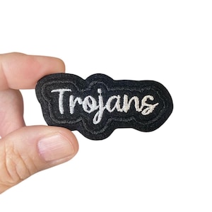 May include: Black embroidered patch with white lettering that reads "Trojans".