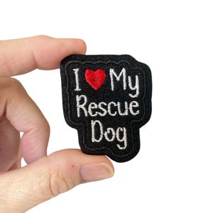 May include: Black felt patch with white embroidery that reads "I love my rescue dog" with a red heart in place of the word "love".