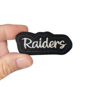 May include: Black embroidered patch with white lettering that reads "Raiders".