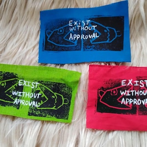 May include: Three rectangular fabric patches in blue, green, and red. Each patch features a black rectangular block print with a white line drawing of two fish facing each other and the white text "EXIST WITHOUT APPROVAL" centred.