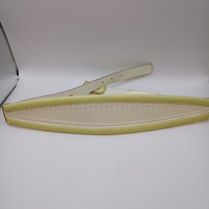 May include: A pale yellow belt with a cream interior and a white strap. The belt features a gold buckle and a textured, snake-like pattern on the interior.