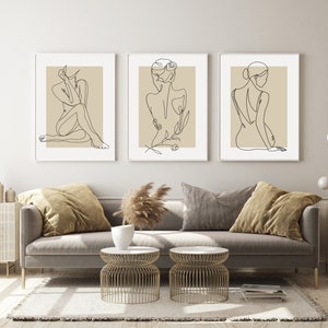Puede incluir: Tres impresiones minimalistas de arte lineal con figuras femeninas en varias poses. Las impresiones est&aacute;n enmarcadas en blanco y tienen un fondo beige.
