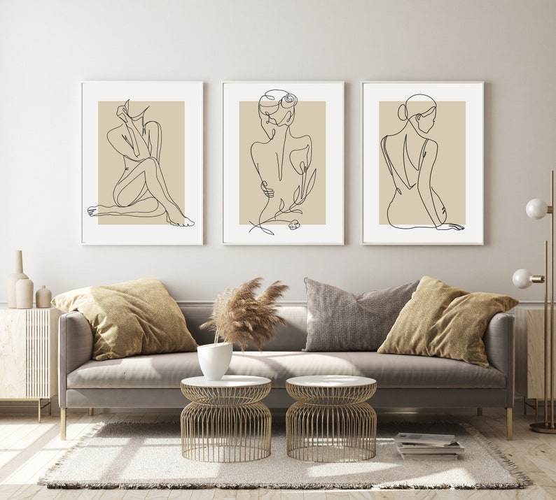 Puede incluir: Tres impresiones minimalistas de arte lineal con figuras femeninas en varias poses. Las impresiones est&aacute;n enmarcadas en blanco y tienen un fondo beige.
