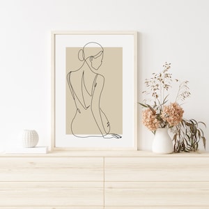 Puede incluir: Una impresi&oacute;n enmarcada de arte lineal de una mujer sentada de espaldas al espectador. El fondo de la impresi&oacute;n es de color marr&oacute;n claro. La impresi&oacute;n est&aacute; colgada en una pared blanca sobre una c&oacute;moda de madera.