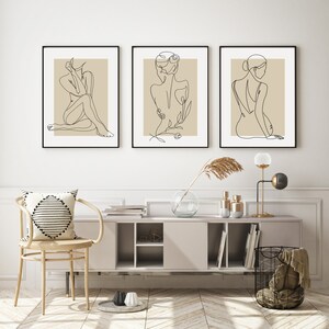 Puede incluir: Tres impresiones minimalistas de arte lineal que presentan una figura desnuda en varias poses. Las impresiones est&aacute;n enmarcadas en negro y tienen un fondo beige.