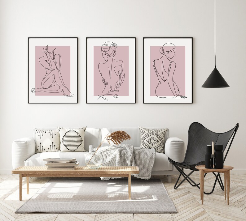 Pu&ograve; includere: Tre stampe minimaliste di arte lineare di una persona in varie pose su uno sfondo rosa. Le stampe sono incorniciate in nero e appese a un muro bianco.