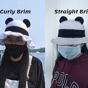 May include: Two crocheted bucket hats with panda ears. The hat on the left has a curly brim and the hat on the right has a straight brim. Both hats are white with a black stripe and black panda ears.