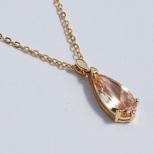 May include: A gold chain necklace with a pear-shaped peach-colored gemstone pendant.