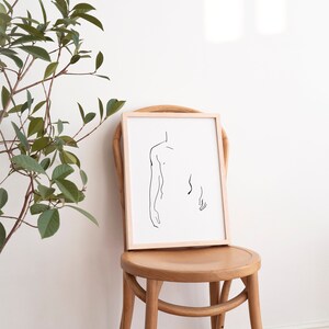 Pu&ograve; includere: Un disegno a linea in cornice di una figura nuda in una cornice di legno semplice, seduto su una sedia di legno contro un muro bianco.