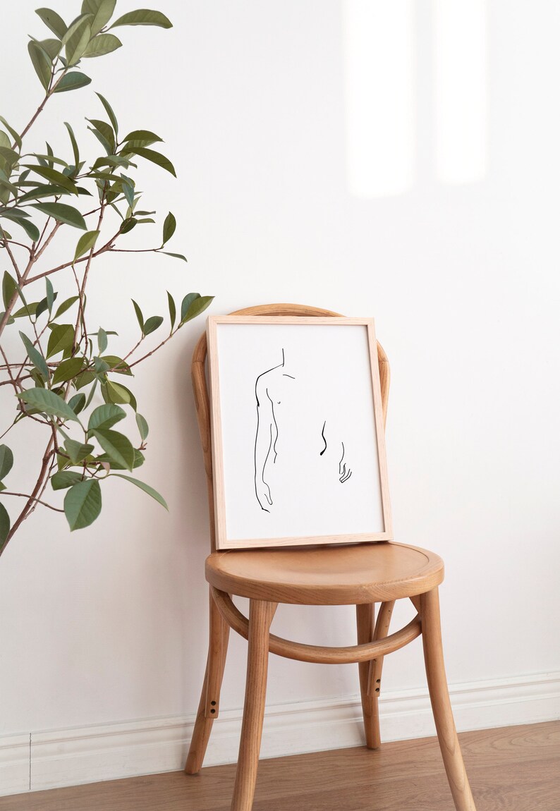 Pu&ograve; includere: Un disegno a linea in cornice di una figura nuda in una cornice di legno semplice, seduto su una sedia di legno contro un muro bianco.