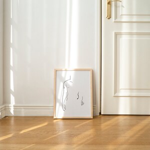 Pu&ograve; includere: Un disegno a linea nera e bianca incorniciato di una persona di spalle, appeso a una parete bianca in una stanza con pavimento in legno e una porta bianca.