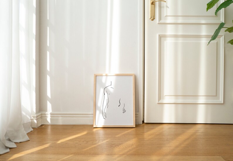 Pu&ograve; includere: Un disegno a linea nera e bianca incorniciato di una persona di spalle, appeso a una parete bianca in una stanza con pavimento in legno e una porta bianca.