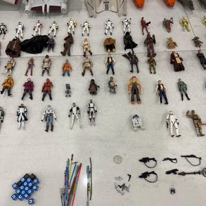 以下が含まれることがあります： スターウォーズのアクションフィギュアと玩具のコレクション。Xウィング戦闘機、様々な宇宙船、多数のキャラクターフィギュアが含まれています。フィギュアは明るい色の表面に配置され、ライトセーバーやサイコロなどのアクセサリーも含まれています。