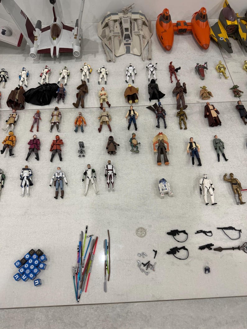 以下が含まれることがあります： スターウォーズのアクションフィギュアと玩具のコレクション。Xウィング戦闘機、様々な宇宙船、多数のキャラクターフィギュアが含まれています。フィギュアは明るい色の表面に配置され、ライトセーバーやサイコロなどのアクセサリーも含まれています。