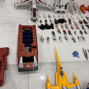 以下が含まれることがあります： 様々な宇宙船とアクションフィギュアを含む、スターウォーズのおもちゃのコレクション。宇宙船は赤、白、黄色、グレーの色合いです。アクションフィギュアは、スターウォーズフランチャイズの様々なキャラクターです。
