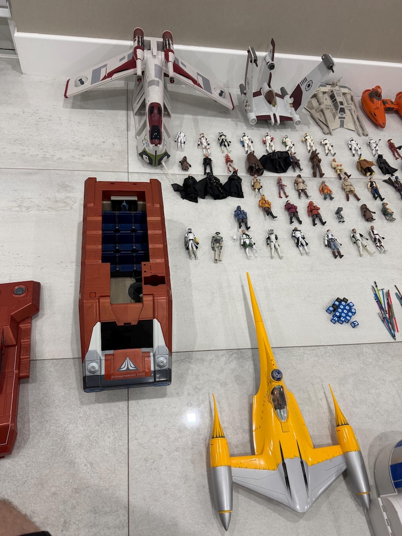 以下が含まれることがあります： 様々な宇宙船とアクションフィギュアを含む、スターウォーズのおもちゃのコレクション。宇宙船は赤、白、黄色、グレーの色合いです。アクションフィギュアは、スターウォーズフランチャイズの様々なキャラクターです。