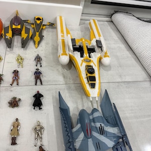 以下が含まれることがあります： スターウォーズのおもちゃのコレクション。宇宙船とアクションフィギュアが含まれています。宇宙船は主に黄色、グレー、白で、詳細なデザインが施されています。アクションフィギュアは、スターウォーズの世界のさまざまなキャラクターを表しています。