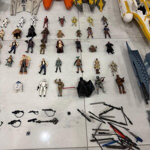 以下が含まれることがあります： スターウォーズのアクションフィギュアと乗り物のコレクション。Xウィング、戦闘機、ダース・ベイダー、ストームトルーパー、ヨーダなどの様々なキャラクターが含まれています。おもちゃは様々なサイズと色で、明るい色の表面に配置されています。