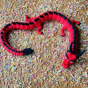 May include: A red and black rubber dragon toy on a background of colorful sprinkles.