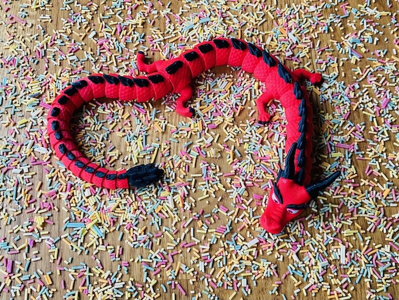 May include: A red and black rubber dragon toy on a background of colorful sprinkles.